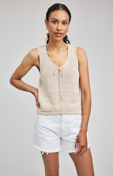 Woman wearing a beige sleeveless top and white shorts on a plain background