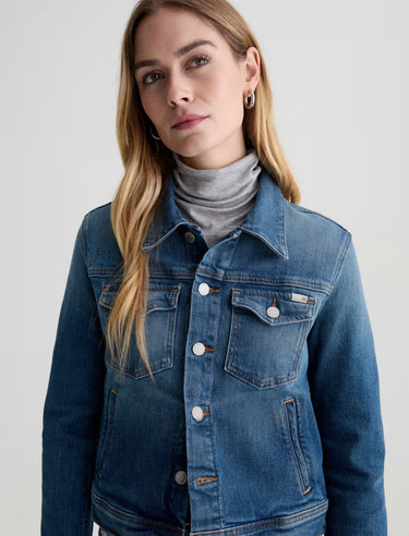 Woman wearing a blue denim jacket over a gray turtleneck on a light gray background