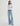Person wearing a white shirt and light blue jeans with a belt on a plain background
