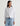 Person wearing a white denim jacket and light blue jeans on a plain background