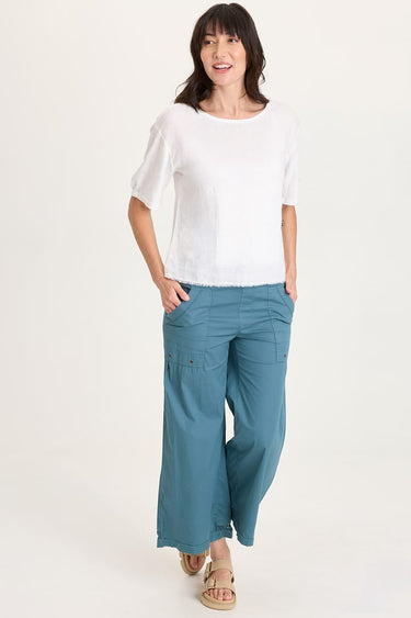 Woman wearing a white top and teal pants on a white background