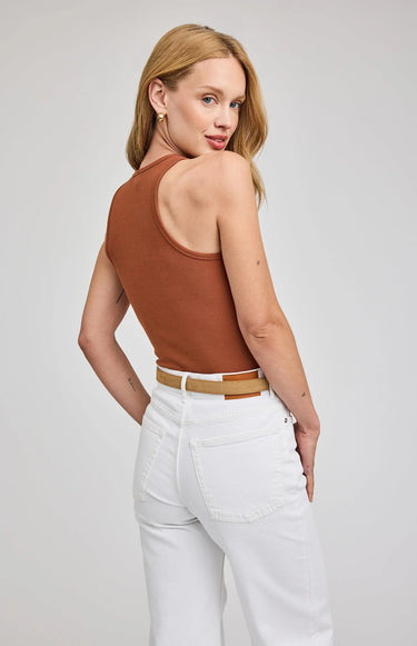 Woman wearing a brown tank top and white pants on a plain background