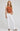 Woman wearing a brown tank top and white pants on a plain background