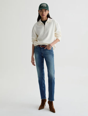 Person wearing a white sweater, blue jeans, and brown boots on a white background