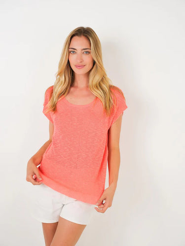 Woman wearing a coral top and white shorts on a white background