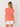 Woman wearing a coral sweater and white shorts on a plain background