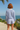 Person wearing a striped shirt and shorts standing on a path with ocean and sky in the background