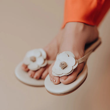 White sandals with floral designs worn by a person on a beige background
