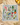 A square embroidered bandana with a colorful Mediterranean-themed design, laid flat on a beige fabric surface with styled props including lemons, a glass, and dried flowers.