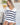 Woman in a striped sweater holding a glass of white wine indoors.