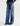 A person wearing blue wide-leg denim jeans with a dark navy long-sleeve top and dark brown shoes, standing against a plain light gray studio background.