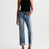 A model wearing light-wash blue cropped jeans with rolled cuffs, a black sleeveless mock-neck top, and black pointed-toe heels, photographed against a plain white studio background.