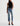 A model wearing light-wash blue cropped jeans with rolled cuffs, a black sleeveless mock-neck top, and black pointed-toe heels, photographed against a plain white studio background.