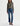 Woman wearing a patterned blouse and mid-rise medium blue wash straight leg denim with a distressed hem, fading, and gold stitching on a white background.