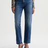 A woman wearing mid-rise medium blue wash straight leg denim with a distressed hem, fading, and gold stitching on a white background.