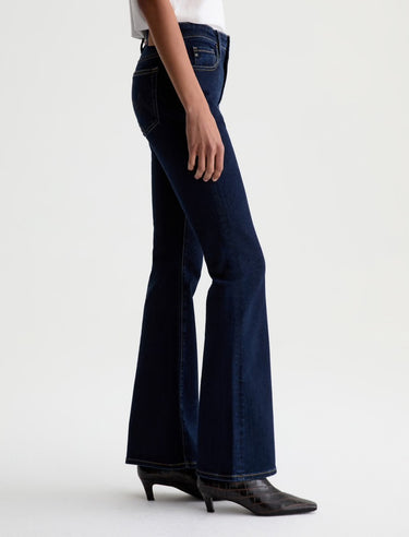 Dark blue flared jeans worn by a person on a white background