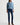 A model wearing a light blue long-sleeve knit polo-collar sweater, dark blue skinny jeans, and brown pointed-toe heeled ankle boots, standing against a plain white studio background.