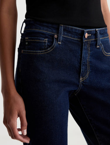 A woman wearing low rise straight dark blue jeans and black heels on a white background.