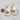 A pair of gold teardrop hoop earrings with white mother-of-pearl teardrop pendants, displayed on a light beige textured surface next to a US dime for scale.