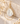 A teardrop-shaped gold hoop earring with a milky white mother-of-pearl stone, styled on a beige stone slab with dried flowers.