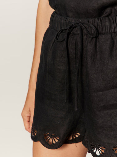 A close up view of a black linen shorts with scalloped edges on a neutral background 