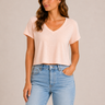 A woman wearing a light pink cropped v neck tee and jeans on a neutral background