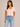 A woman wearing a light pink cropped v neck tee and jeans on a neutral background
