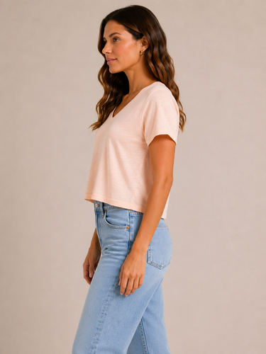 A woman wearing a light pink cropped v neck tee and jeans on a neutral background