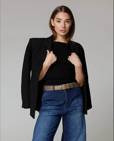Woman wearing a black blazer, black top, and blue jeans on a gray background