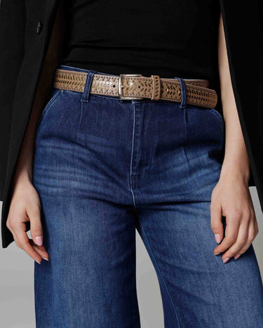 Person wearing blue jeans with a decorative belt on a neutral background