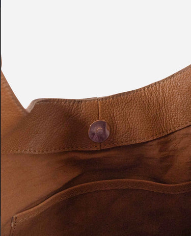 Close-up of a brown leather shoulder bag showing the pebbled texture, stitched edge, and a single round button closure against a plain white background.