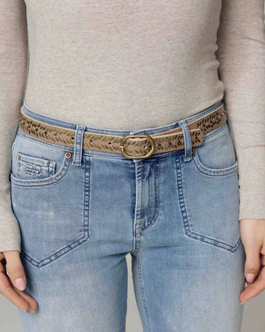 Person wearing light blue jeans with a patterned belt and beige sweater.