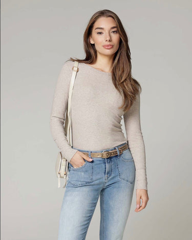 Woman wearing a beige sweater and light blue jeans against a gray background