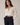 A woman wearing a cream-colored long-sleeve button-down shirt tucked into dark navy trousers, accessorized with a brown leather belt with a silver buckle, against a neutral beige background.