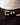 A close-up of a black leather belt with a polished gold-tone buckle, worn with dark trousers and a white ribbed top.