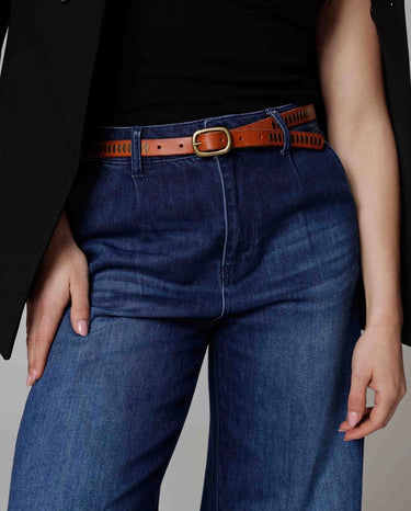Person wearing blue jeans with a brown belt on a neutral background