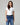 Woman wearing a white t-shirt and blue jeans with a black belt against a gray background