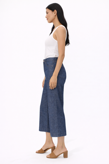 a woman wearing a white tank and dark cropped jeans standing to the side