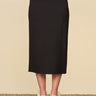 a woman wearing a black pencil midi skirt and beige heels on a neutral background