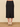 a woman wearing a black pencil with a center slit in the back of the midi skirt and beige heels on a neutral background