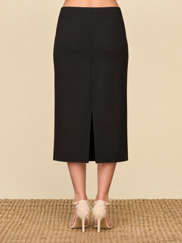 a woman wearing a black pencil with a center slit in the back of the midi skirt and beige heels on a neutral background