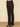 Black high-waisted straight-leg pants shown on a model from the waist down, paired with black pointed-toe heels on a textured beige woven rug against a solid beige background.
