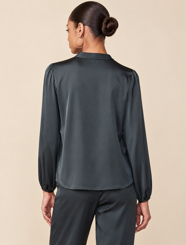 A woman shown from the back wearing a dark green satin blouse with long balloon sleeves and matching satin trousers, set against a solid beige background.