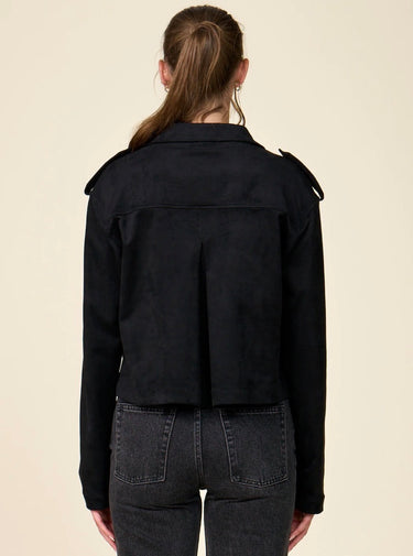 A woman modeling a black double-breasted cropped jacket paired with dark black jeans, against a solid light beige background.