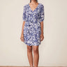 Woman wearing a blue floral dress standing on a woven mat with a beige background