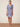 Woman wearing a blue floral dress standing on a woven mat with a beige background