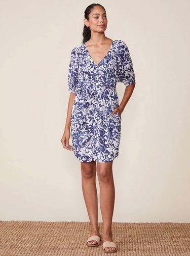 Woman wearing a blue floral dress standing on a textured surface with a neutral background