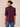A woman shown from the back wearing a dark plum purple blouse with puff sleeves and ruffled cuffs, paired with blue jeans, against a solid beige background.