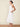Woman wearing a white dress standing against a beige background