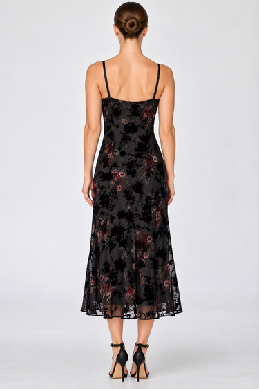 a woman wearing a black dress with lace along the neckline and colorful floral velvet detailing.